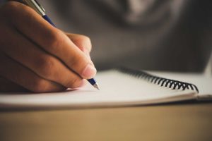 خودکار در دست یک مرد روی دفتر در حال سناریونویسی تبلیغاتی